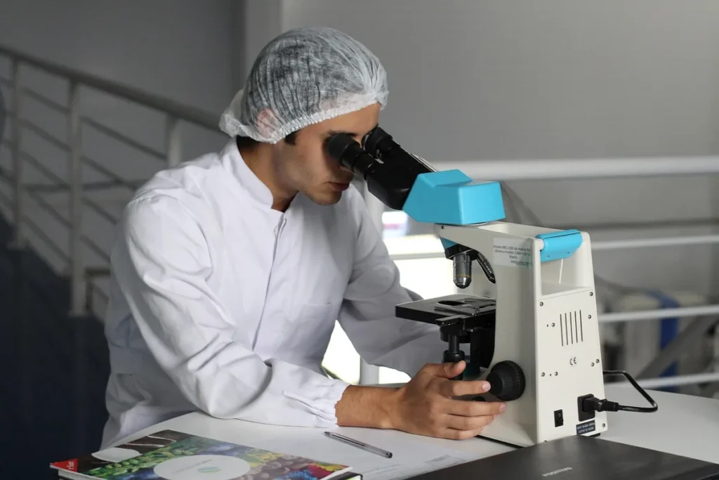Badacz w fartuchu pracuje przy mikroskopie w laboratorium