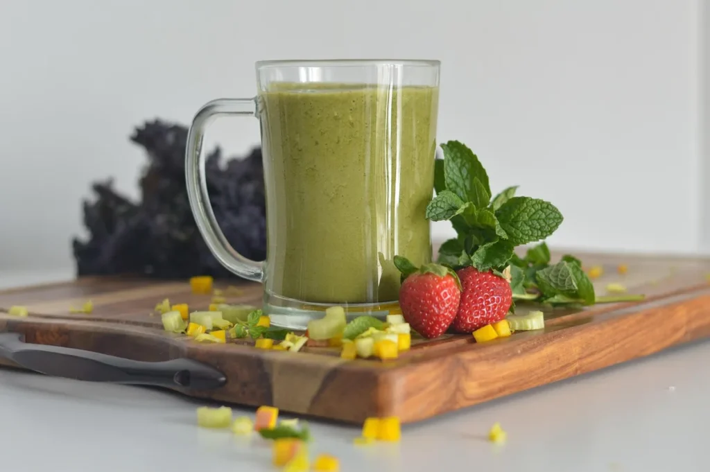 Zielone smoothie w kuflu na desce obok truskawek i mięty: detoks sokowy