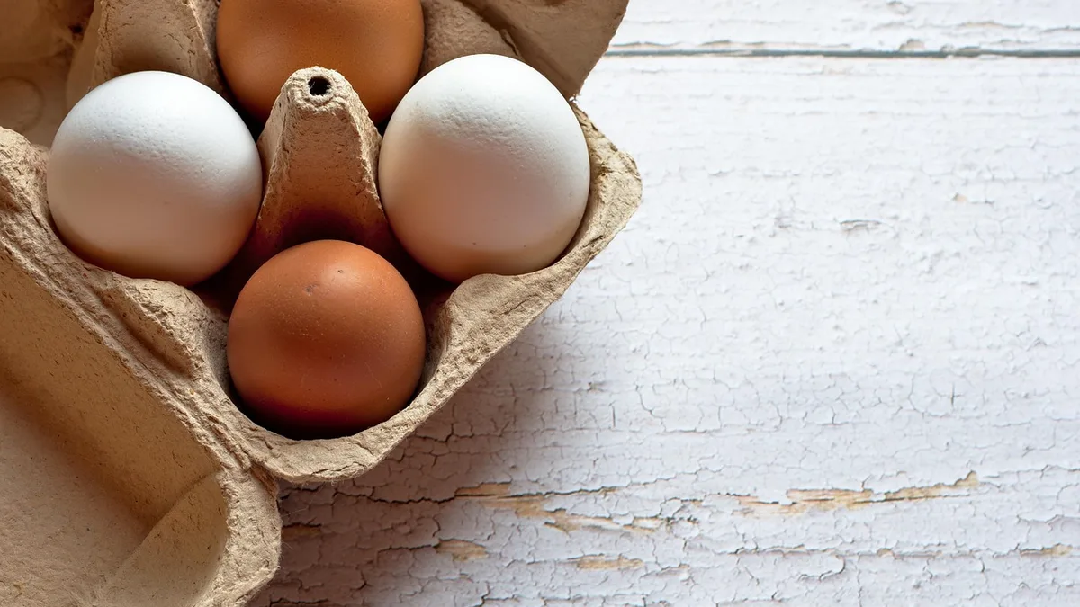 Białe i brązowe jajka w kartonie na jasnym drewnianym stole: jajka a cholesterol
