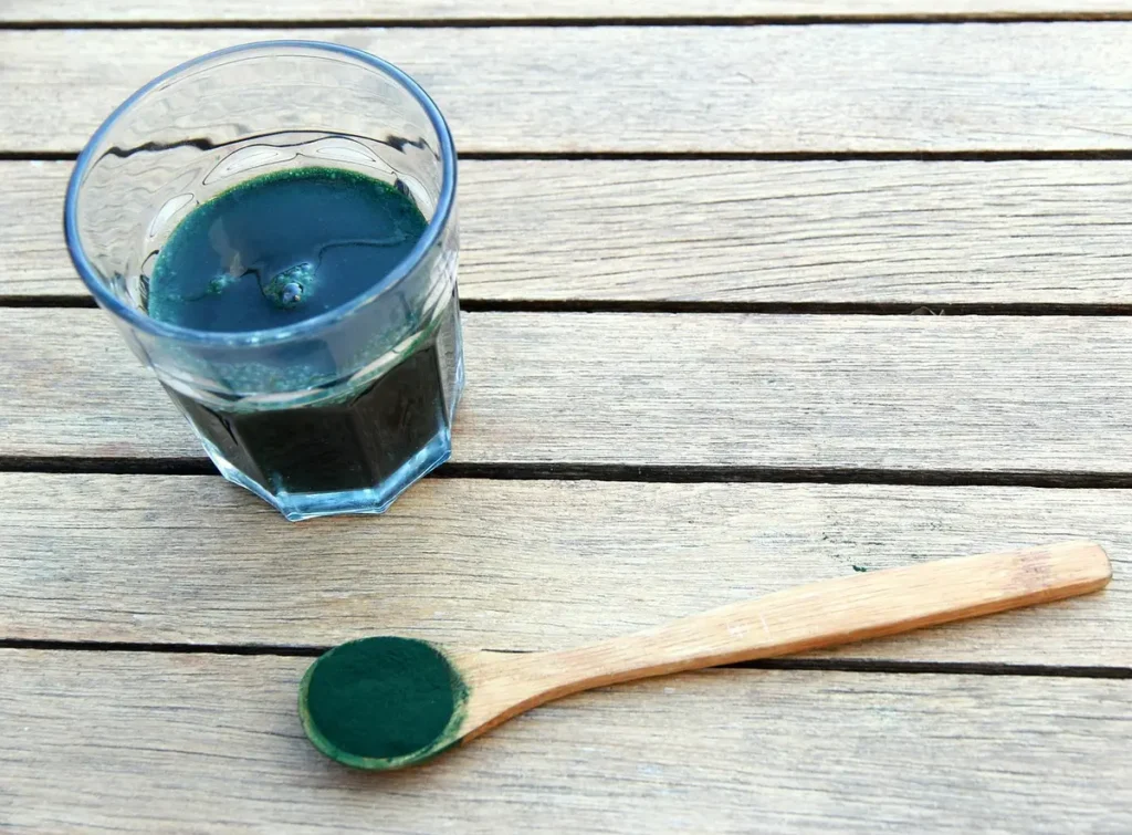 Szklanka z rozmieszaną spiruliną i drewniana łyżka proszku na stole